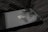 A close-up view of a sleek, black smartphone with Apple's logo on its back panel. The phone is resting on a dark, striped fabric surface. The dual camera setup on the phone is prominently visible.