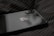 A close-up view of a sleek, black smartphone with Apple's logo on its back panel. The phone is resting on a dark, striped fabric surface. The dual camera setup on the phone is prominently visible.