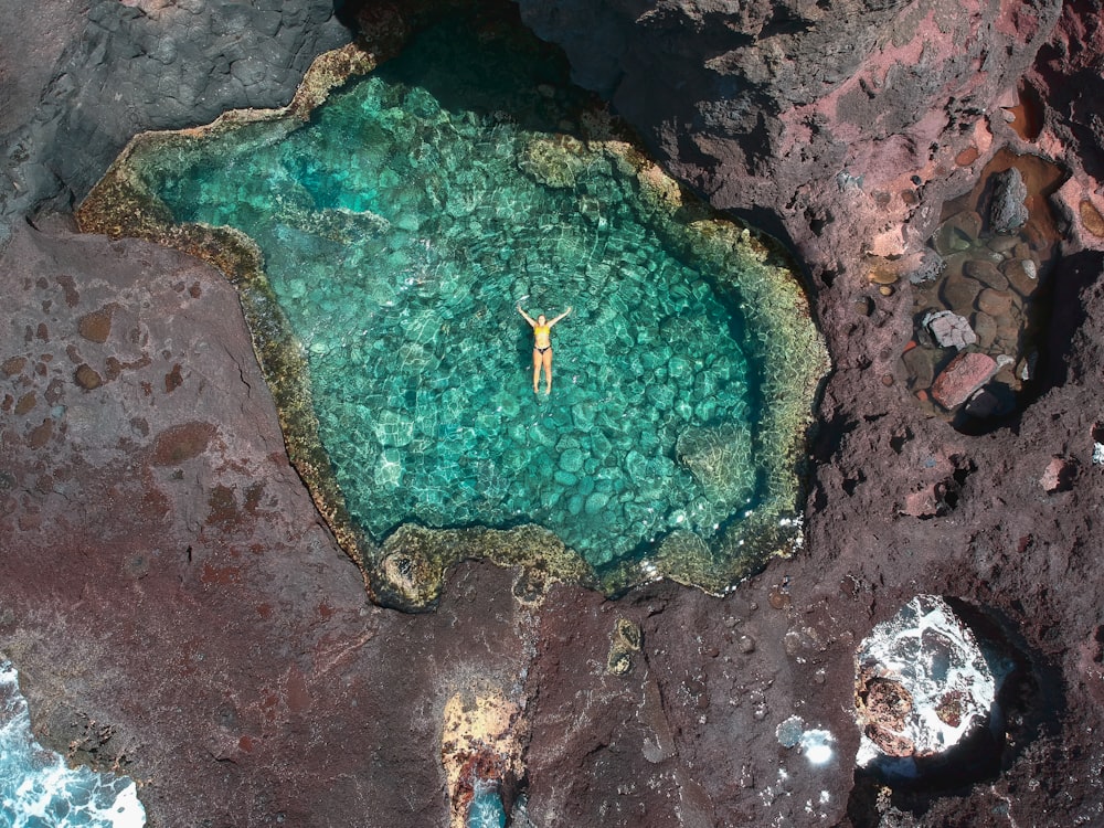 Fotografía aérea de una persona flotando en el cuerpo tranquilo del lago rodeado de roca durante el día