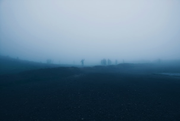 A misty riverbank at twilight with shadowy figures barely visible through the fog.