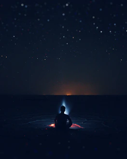 A peaceful meditation scene with a person sitting cross-legged under a starry cosmic sky, third eye illuminated.