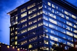 Evening view of a completed office tower with reflective glass windows illuminated by city lights.