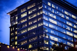 Exterior view of a sleek office building at dusk with illuminated windows.