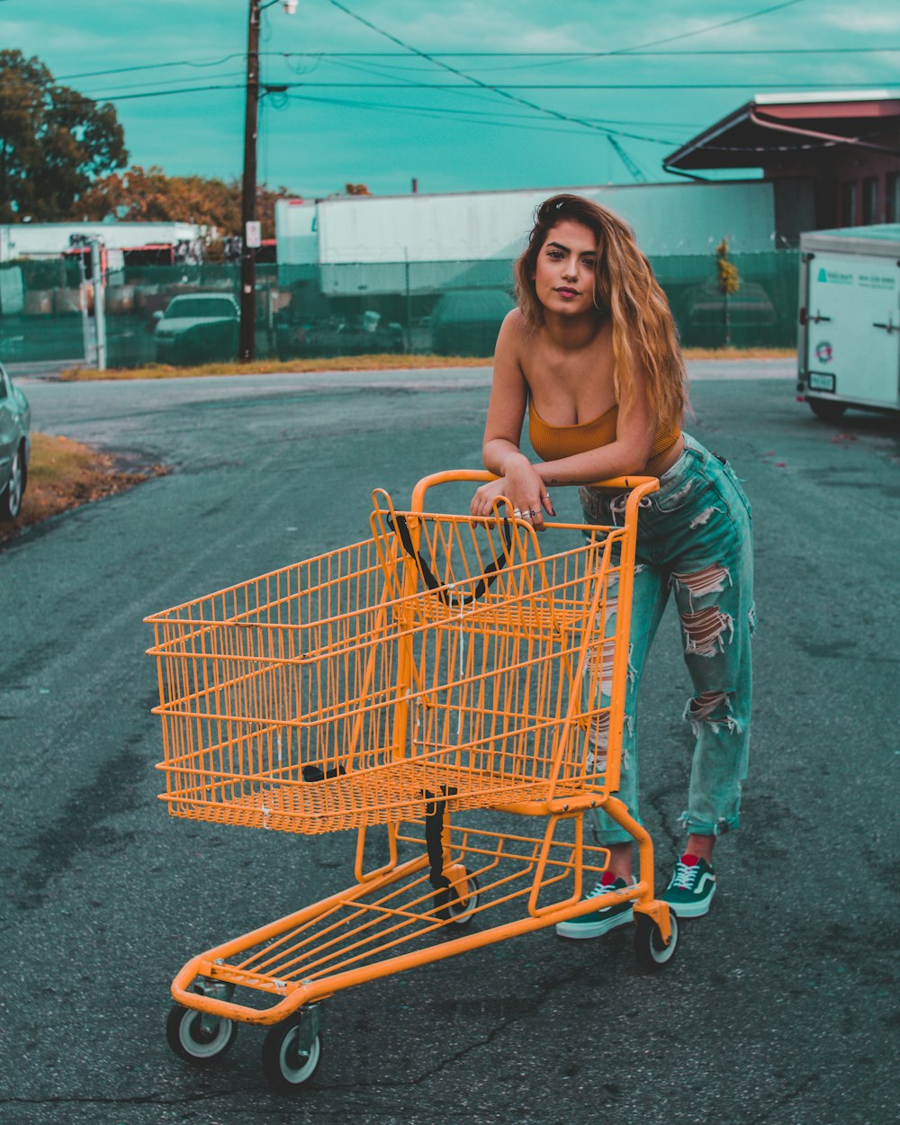 Frau lehnt sich an gelben Einkaufswagen und steht tagsüber auf Betonpflaster