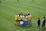 A group of female soccer players, wearing yellow and white jerseys, stands in a tight huddle on a lush green soccer field. The players are focused and engaged, suggesting they are discussing strategies or motivating each other. Nearby, two coaches in black sportswear observe and provide guidance.