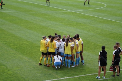Women rugby players huddled together on a sunny field, showing team spirit and focus.