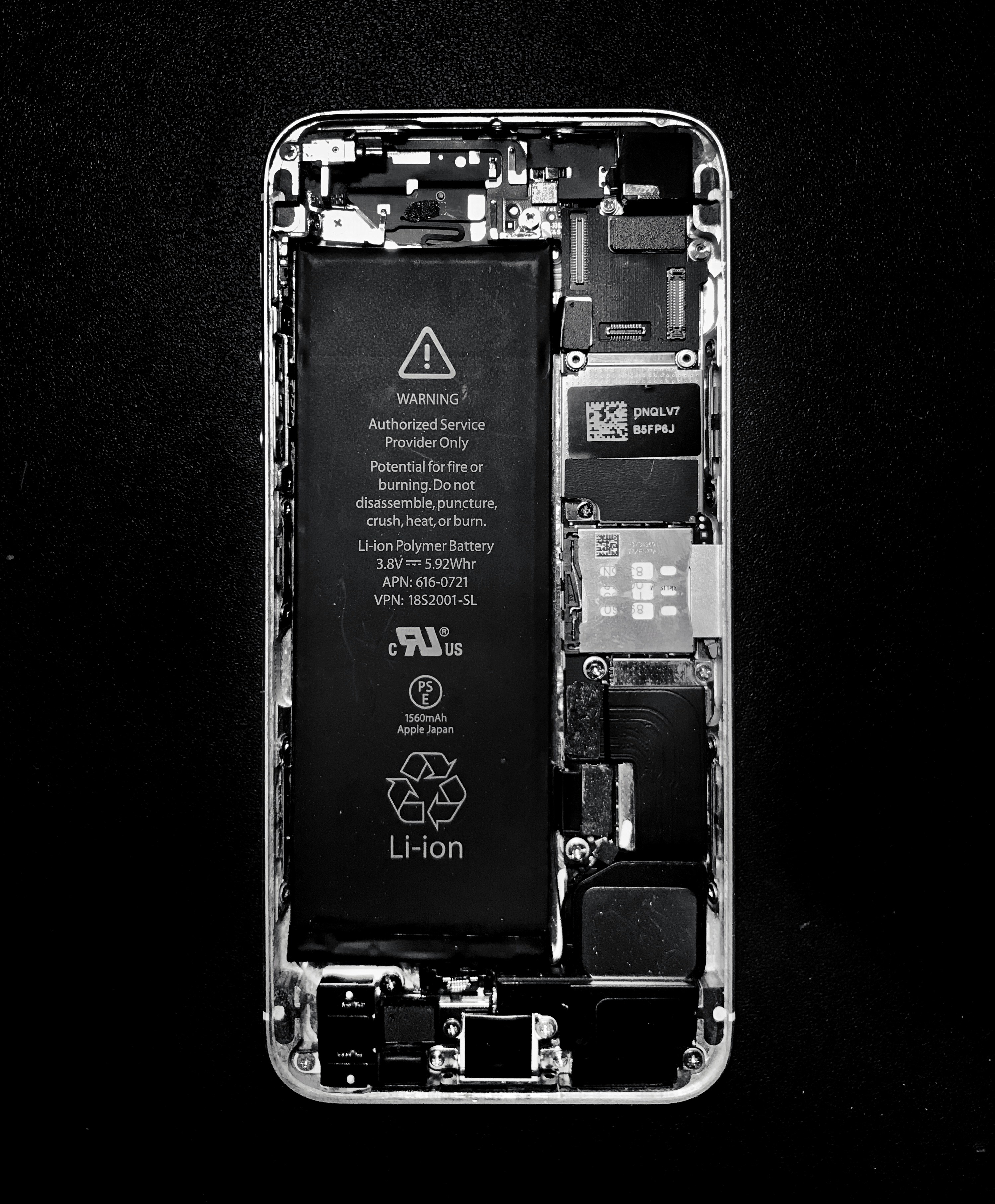 Close-up of phone battery being removed from device under bright workshop lighting showing internal components