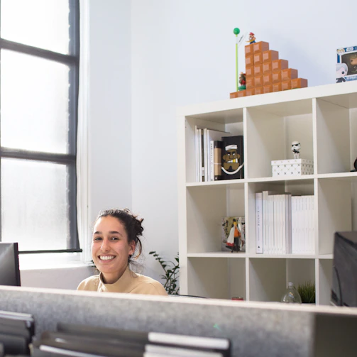 A smiling person sitting at a desk with real estate documents, looking proud and focused in a cozy home office.