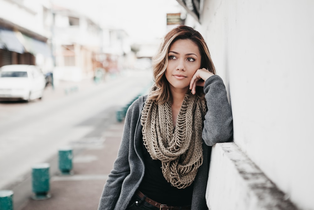 woman in gray coat leaning on white wall