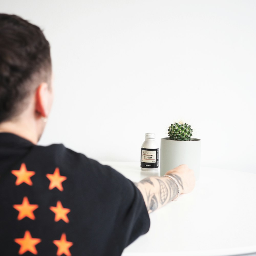person holding round white ceramic pot with green succulent on top of white table