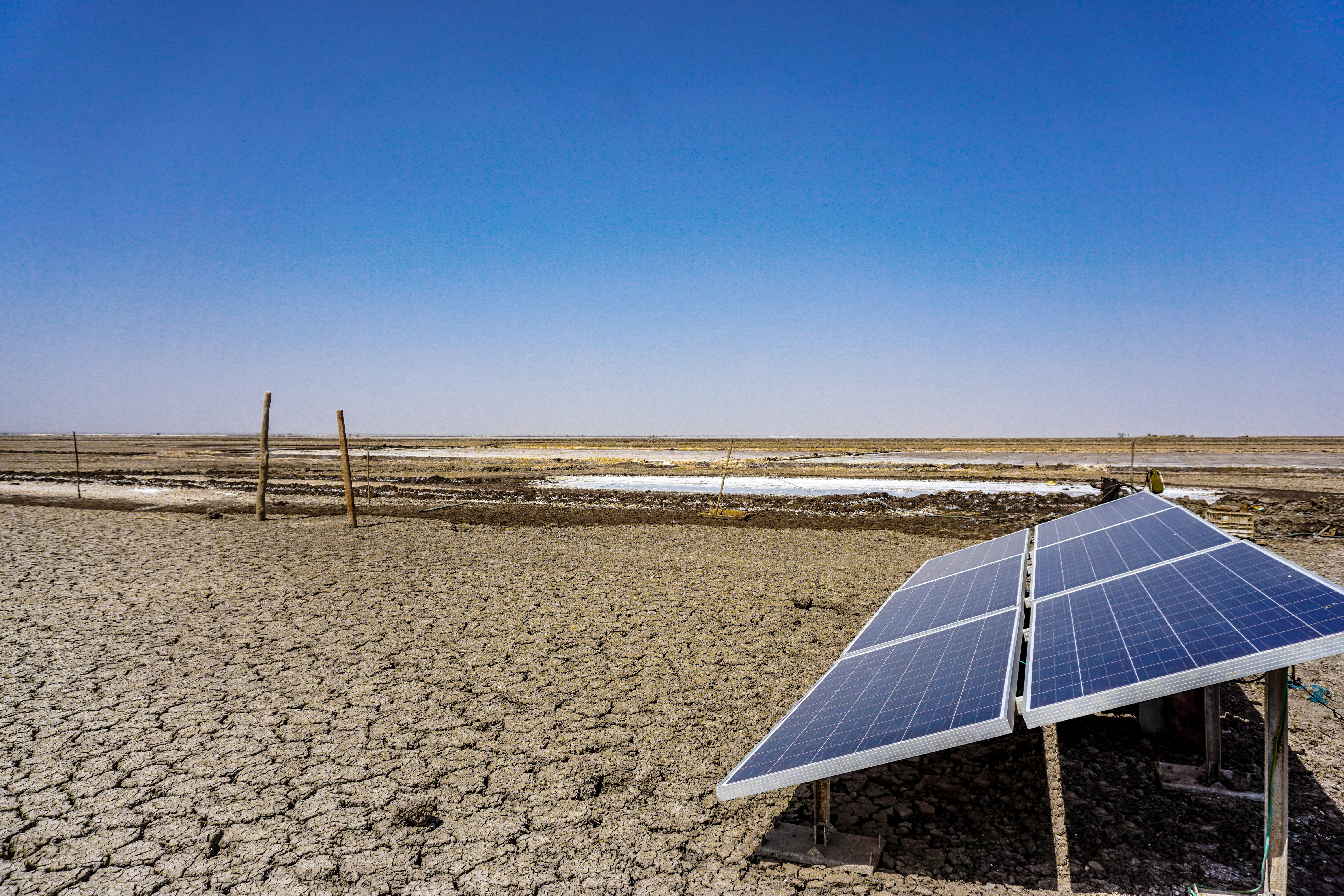 Portable solar panel laid flat on dry earth in a desert landscape, warm golden light, sparse vegetation