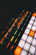 A close-up view of a digital music production device featuring a brightly lit interface with colorful buttons and a display screen showing frequency and resonance settings.