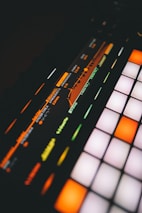 A close-up view of a digital music production device featuring a brightly lit interface with colorful buttons and a display screen showing frequency and resonance settings.