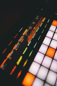 A close-up view of a digital music production device featuring a brightly lit interface with colorful buttons and a display screen showing frequency and resonance settings.
