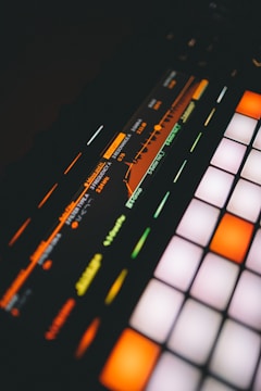 A close-up view of a digital music production device featuring a brightly lit interface with colorful buttons and a display screen showing frequency and resonance settings.
