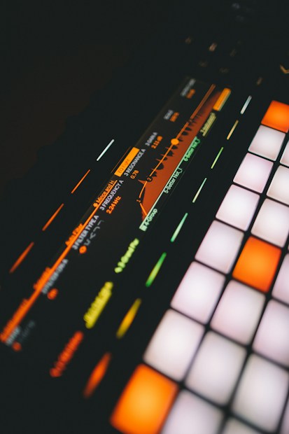 A close-up view of a digital music production device featuring a brightly lit interface with colorful buttons and a display screen showing frequency and resonance settings.