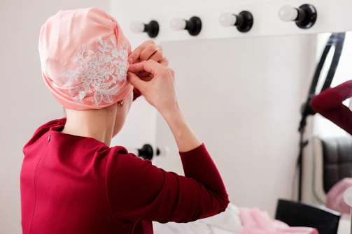 A candid photo of a woman adjusting her scarf in front of a mirror with soft lighting.