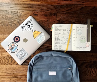 flat lay photography of blue backpack beside book and silver MacBook