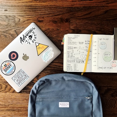 flat lay photography of blue backpack beside book and silver MacBook