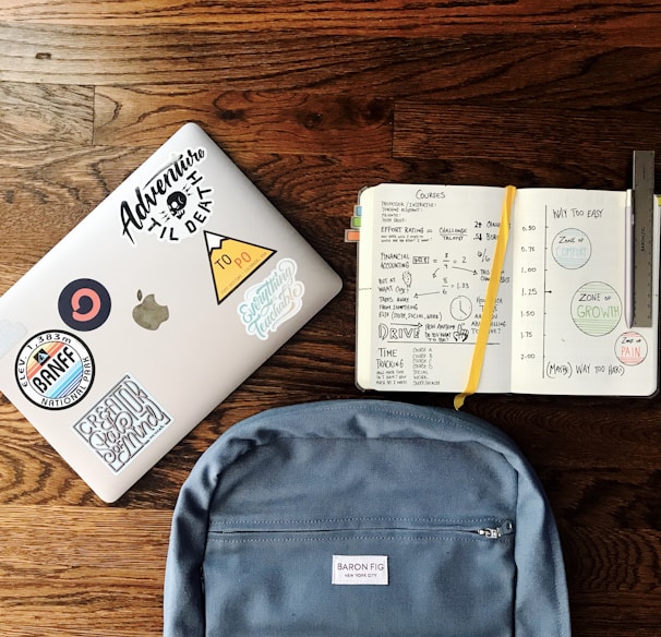 flat lay photography of blue backpack beside book and silver MacBook