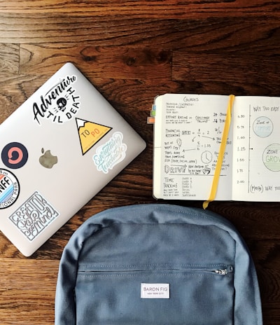 flat lay photography of blue backpack beside book and silver MacBook