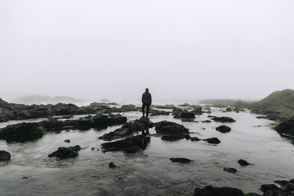 silhouette of person standing on stone surrounded by water during daytime