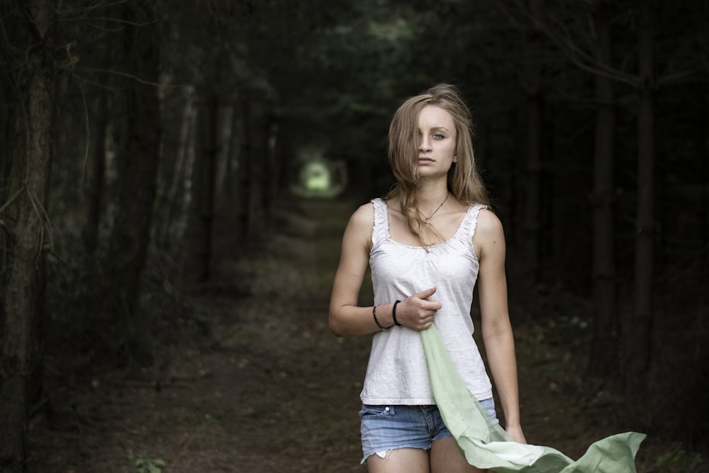 woman wearing white sleeveless top and blue denim short shorts standing on pavement between trees at day