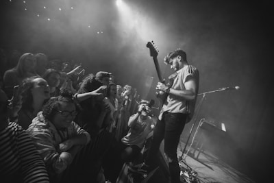 Close-up of a guitar player on stage with fans reaching out in excitement.