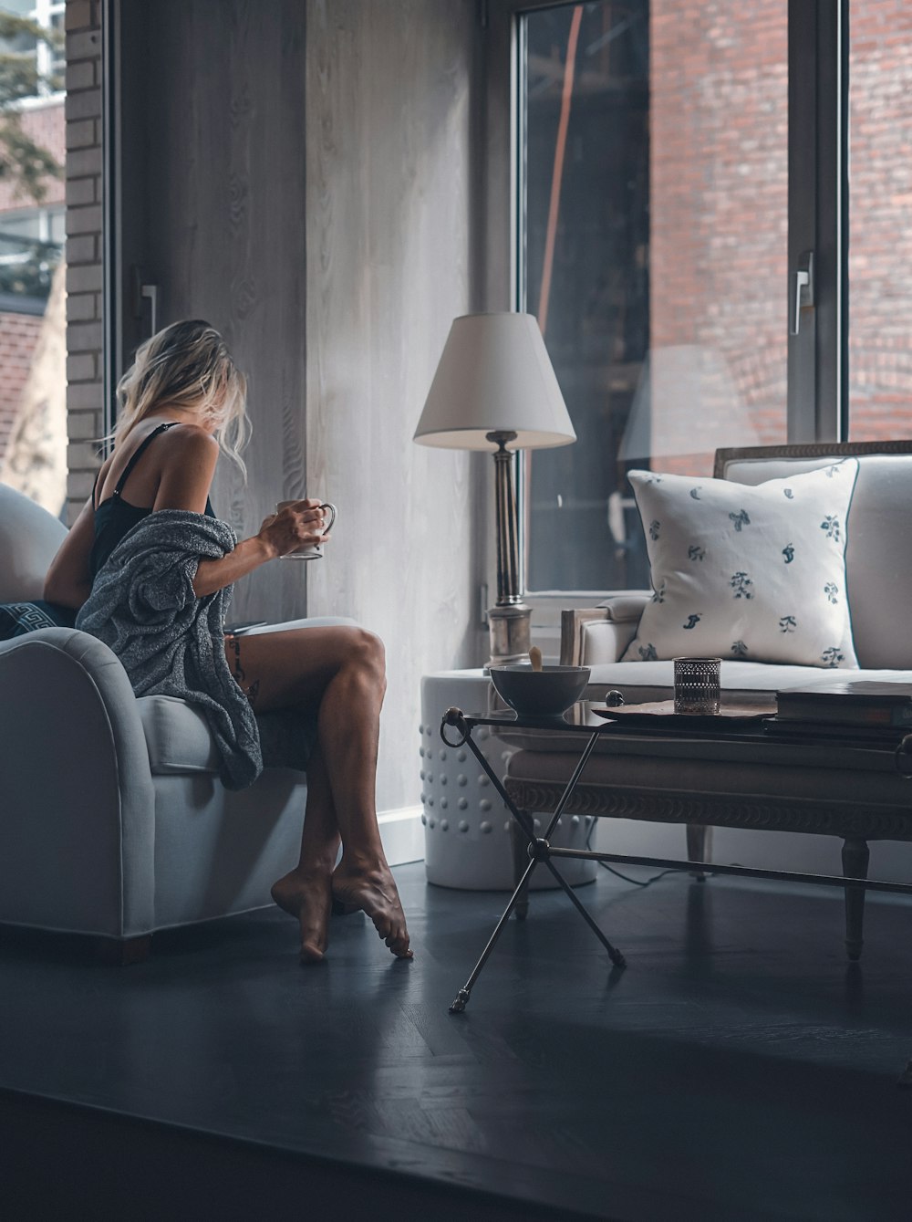 マグカップを持って灰色のソファの椅子に座っている女性