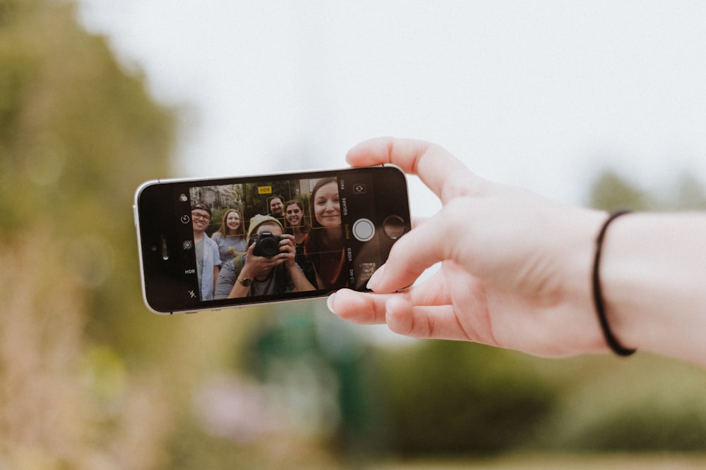 persona che tiene l'iPhone SE grigio spazio che mostra l'uomo che tiene la fotocamera