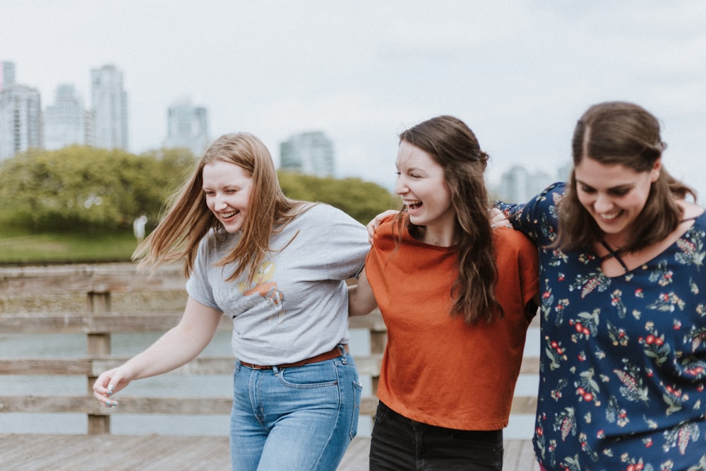 three women walking on brown wooden dock near high rise building during daytime