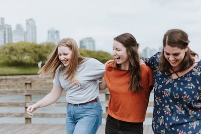 three women walking on brown wooden dock near high rise building during daytime