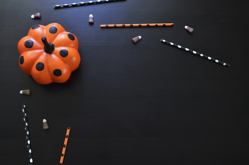 orangefarbenes und schwarzes gepunktetes Kürbisspielzeug auf schwarzem Tisch
