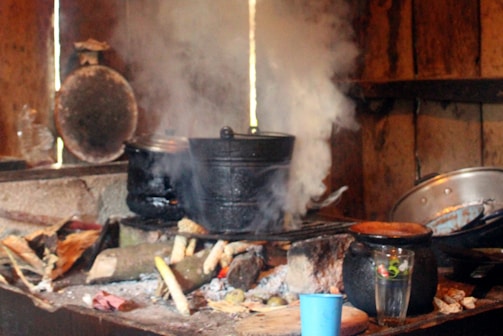 A rustic kitchen scene showing a pot of pilav simmering on the stove with chicken nearby.