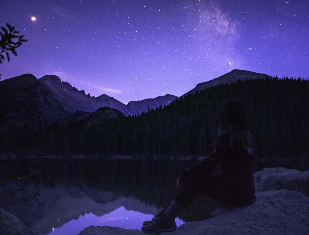 woman sitting on rock near lake facing mountaing