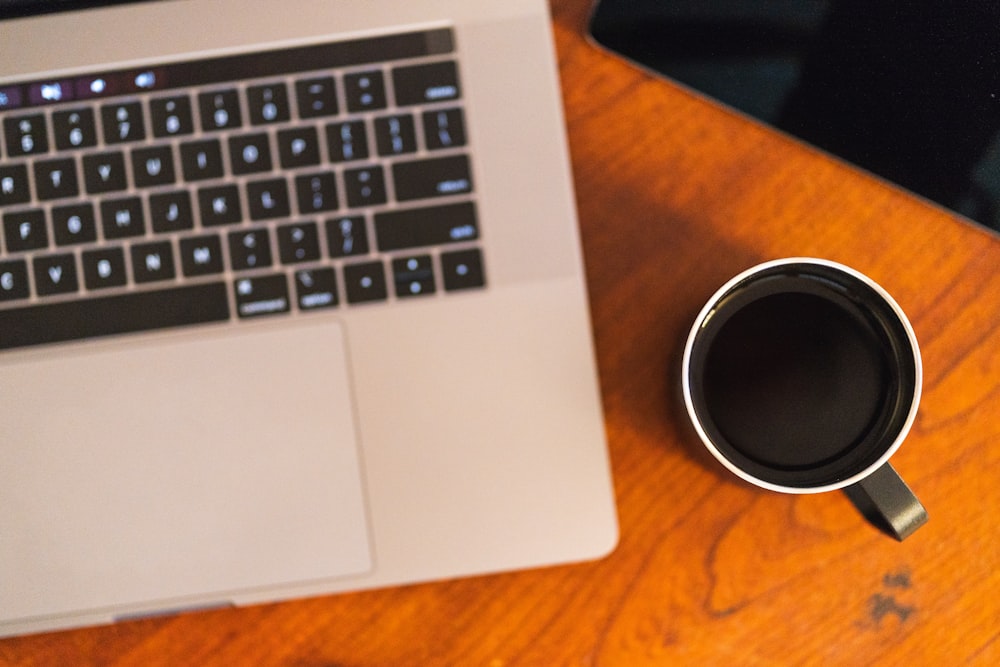 black ceramic mug beside MacBook Pro on brown wooden surface