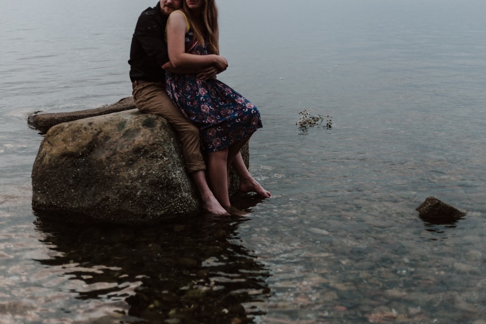 man and woman sitting on rock
