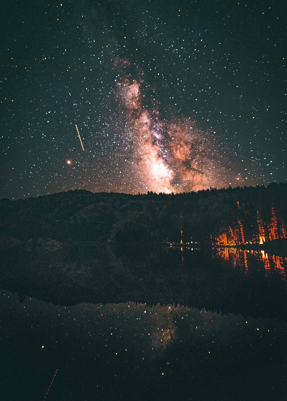 sky phenomenon above pine trees near body of water