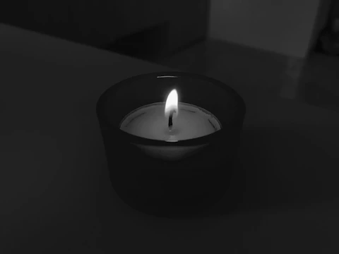 A calming scene of a candle flickering beside a cup of tea on a light ivory desk.