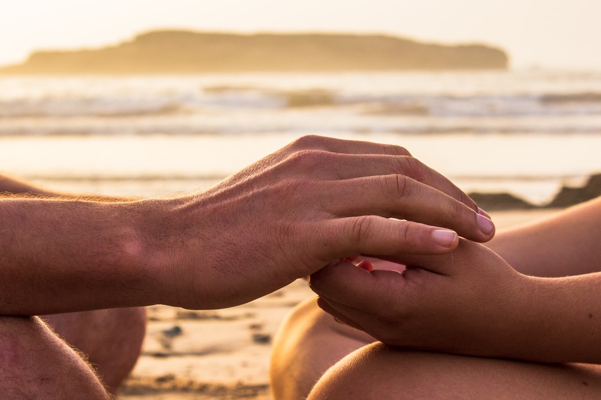 Two people touching hand on a peaceful beach at sunset.