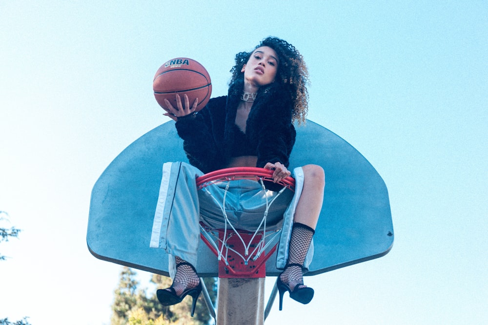 Frau sitzt tagsüber auf Basketballkorb und hält Basketball