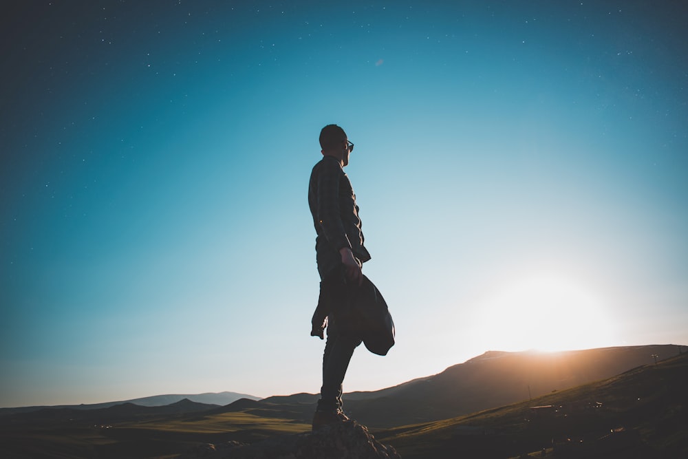 man standing on hill under blue sky