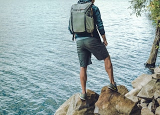 man standing on rock formation in front of calm body of water during daytime