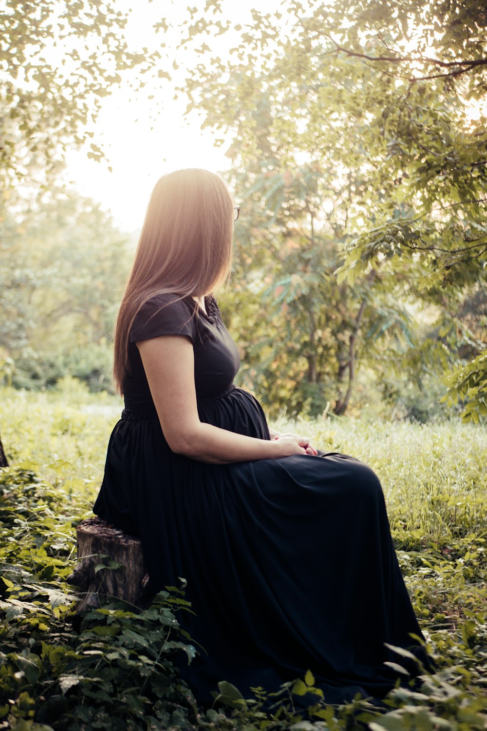 woman sitting on tree stump surrounded by plants