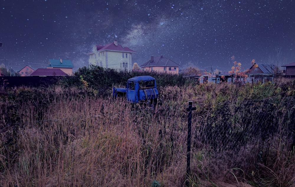 blue vehicle in grass field with houses at distance