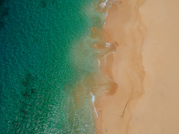 A vibrant drone shot of turquoise ocean waves meeting a golden sandy beach at sunset