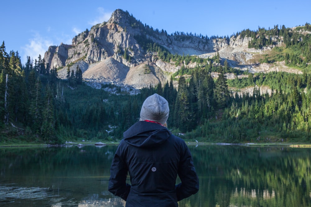 woman standing in front of river and mountain during daytime