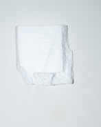 A white, irregularly shaped block of polystyrene foam is positioned centrally against a plain, light background. The texture of the foam is visible, showcasing its porous and slightly rugged surface.