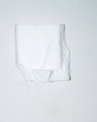 A white, irregularly shaped block of polystyrene foam is positioned centrally against a plain, light background. The texture of the foam is visible, showcasing its porous and slightly rugged surface.