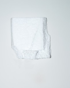 A white, irregularly shaped block of polystyrene foam is positioned centrally against a plain, light background. The texture of the foam is visible, showcasing its porous and slightly rugged surface.